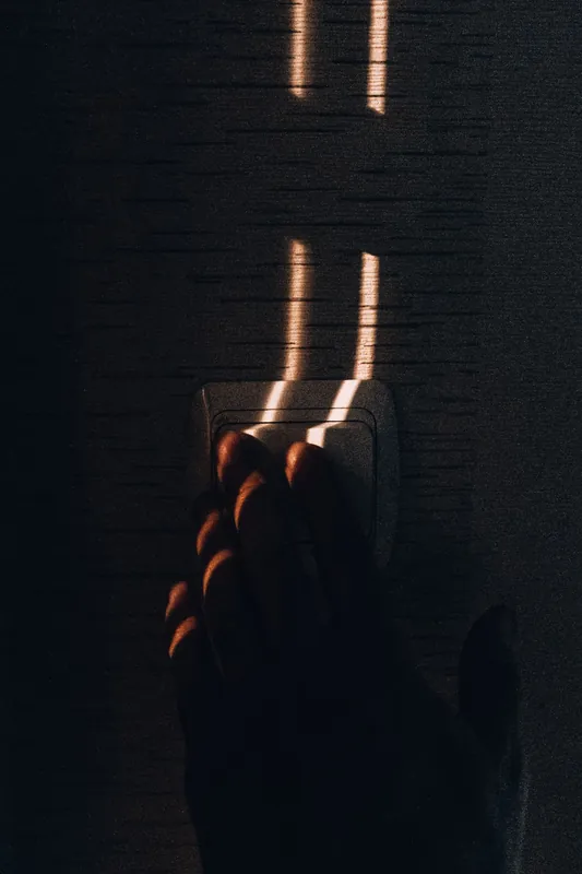 Hand reaching for a wall-mounted dimmer light switch in warm sunlight