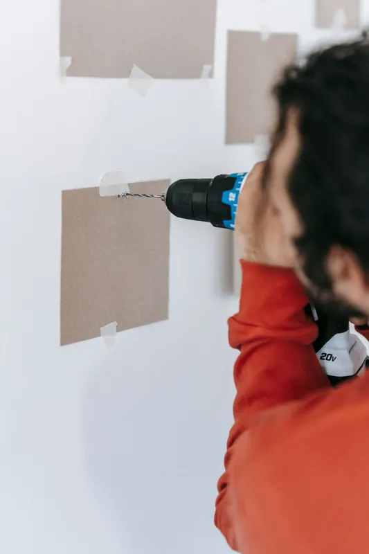 Worker drilling into a wall with a cordless power drill to run new wiring
